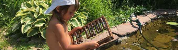 a child dangles its feet in the water and looks at abacus