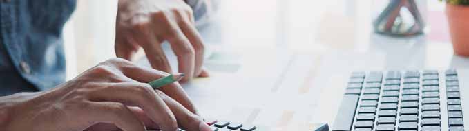 Close up of businessman or accountant hand holding pen working on calculator to calculate business data, accountancy document and laptop computer at office, business concept