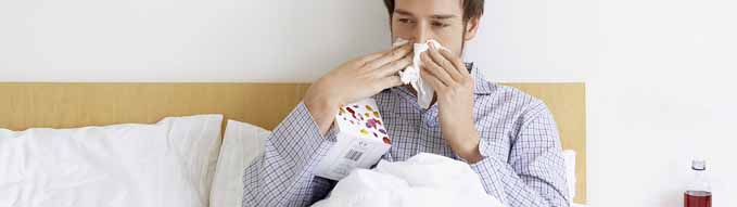 Man with cold in bed blowing nose