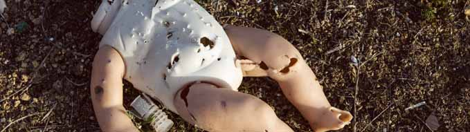 Plastic doll without head with holes from bullets and gun pellets. War aggression