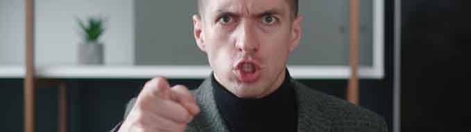 Close-up angry businessman shouting and pointing at camera. Portrait of aggresive boss scolding and shouting at employees threatening with a finger and shouting at the camera.