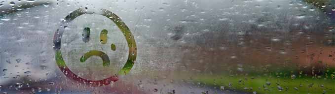 Sad unhappy face drawn on fogged glass on a wet rainy grey window soft light grey skies