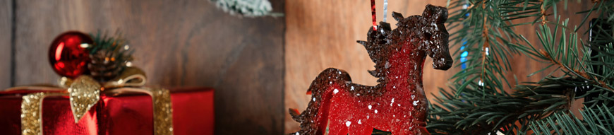 A Christmas tree decoration in the form of a white rocking horse hangs on a pine branch. The horse is a symbol of the new year.