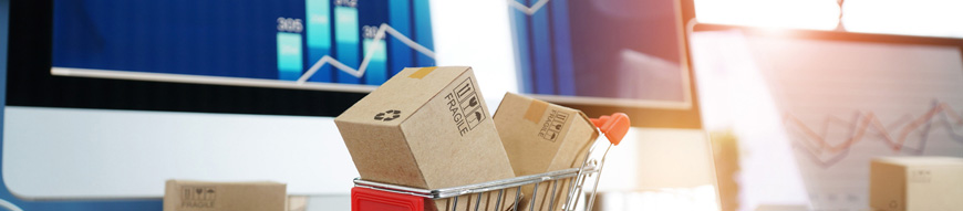 E-commerce. Paper boxes in shopping cart and credit card on keyboard and sales data economic growth graph on computer screen, online shopping and payments, banking, buying and selling services online on network.